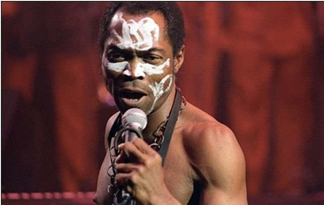 Fela Kuti performing live with his trademark face paint, singing into a microphone