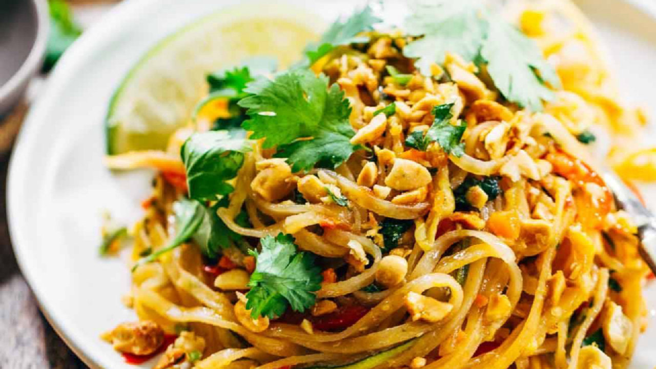 A plate of pad thai with peanuts, coriander and lime