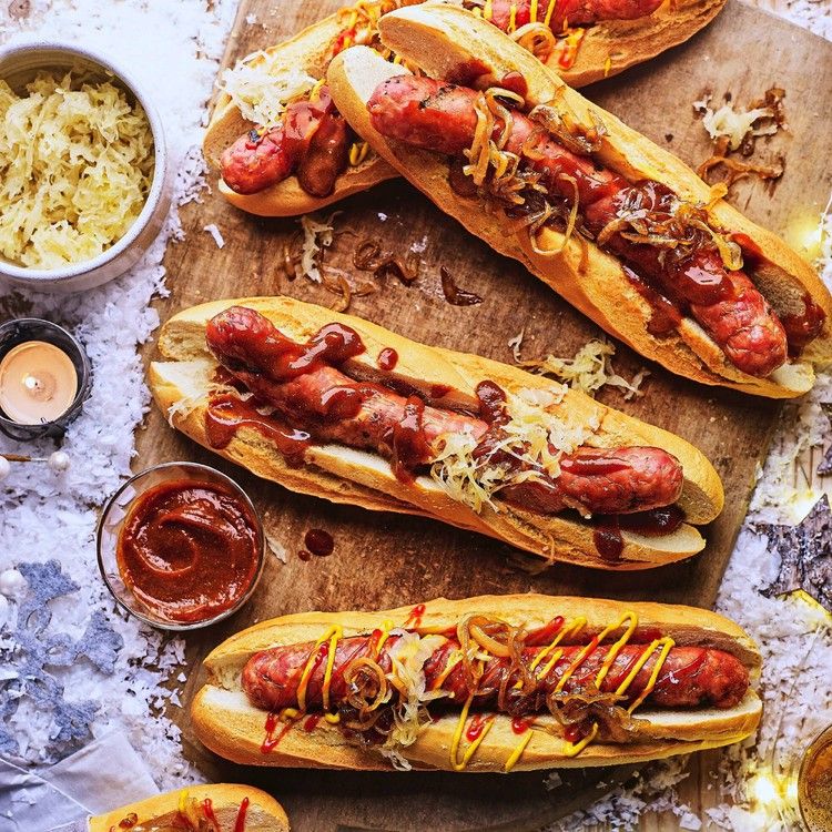 Grilled bratwurst rolls loaded with sauerkraut, fried onions and sauces on a rustic wooden board